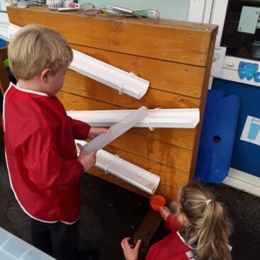 two pupils using rainwater pipes to experiment with water at horton kirby primary school