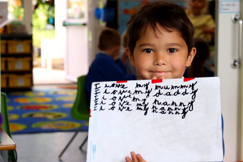 writing-impact pupil in early years foundation stage in english writing on a whiteboard saying how much they love family at horton kirby primary school