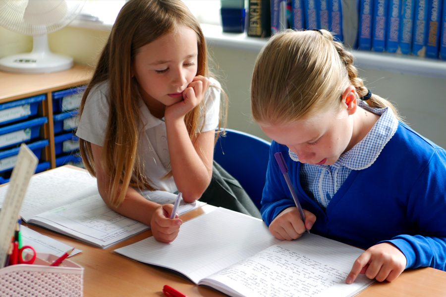 writing-implementation two pupils in english class helping each other with classwork with corrections with purple pens peer assessment at horton kirby primary school