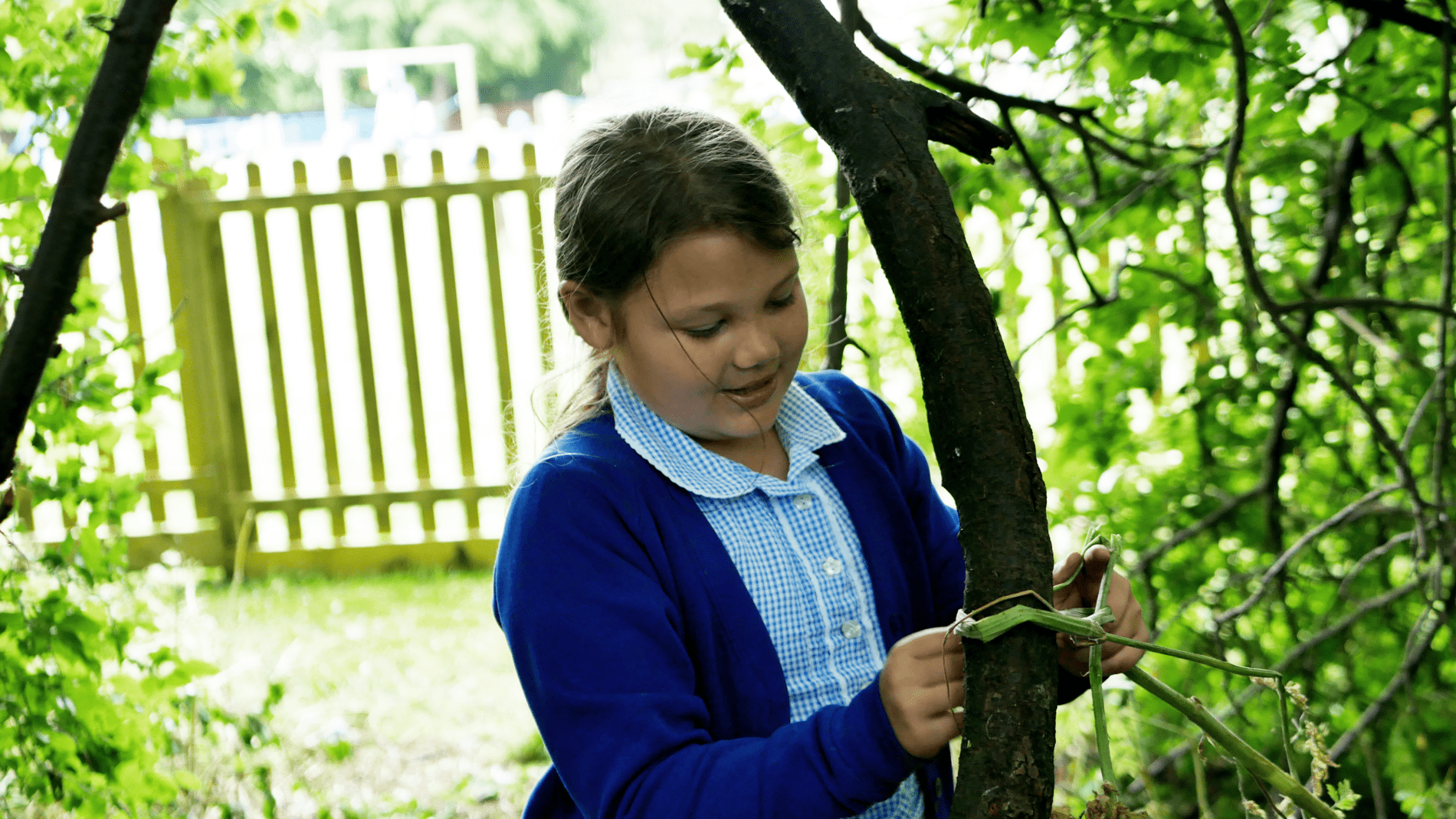 pupil tying leafs to tree trucks as part of forest school at horton kirby primary school